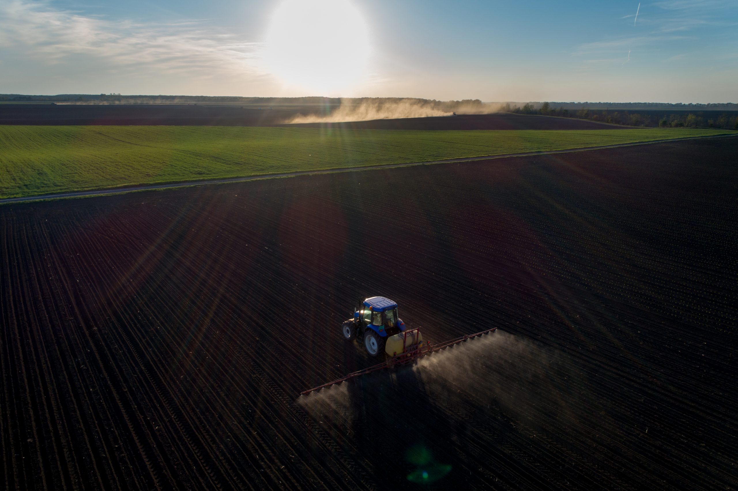 Tractor spraying artificial fertilizer on soil in spring time. Shoot from drone at the evening